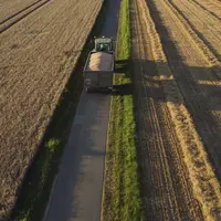 Tracteur avec une benne sur une route au milieu des champs pendant la moisson.