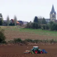 Tracteur semant du  blé à l'autome devant un village.