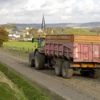 Tracteur tirant une benne agricole laissant de la boue sur une route de campagne
