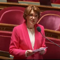 La nouvelle ministre de l'Agriculture Annie Genevard au Sénat, répondant dans un micro à un Sénateur. Mme Genevard porte une veste rose et tient des f