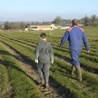 Un homme et un enfant en tenue d'agriculteur marchent dans un champ