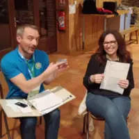 Christine Point-Garion et Denis Beauchamp assis dans une salle avec des papiers à la main. Denis cache ironiquement le code de carte de l'association