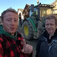 Etienne Fourmont et Jean-Marc Jancovici devant un tracteur dans une cour de ferme.