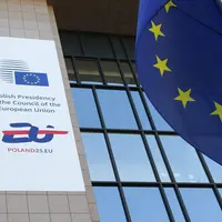 Bannière de la présidence polonaise du Conseil de l'UE sur une partie du bâtiment du Conseil à Bruxelles, avec un drapeau européen au premier plan.