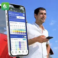 homme tenant un smartphone devant un tracteur dans un champ