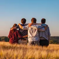 Quatre jeunes de dos se tenant par les épaules au milieu d'un champ.