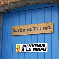 panneau bienvenue à la ferme sur une porte bleue en dessous d'un autre panneau mentionnant salle de traite
