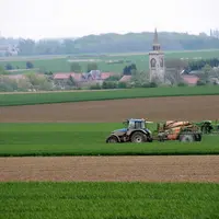 Tracteur fertilisant un champ devant un village