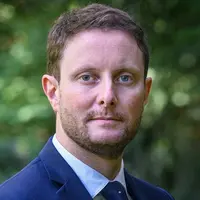 Clément Beaune, Haut-Commissaire à la stratégie et au plan, en gros plan devant un fond de verdure.