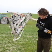 Homme nettoyant une buse dans un champ, machine agricole en arrière-plan