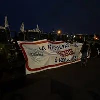 Des tracteurs et agriculteurs avec une banderole sur laquelle est écrit « la révolte paysanne reprend à Versailles »