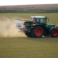 Un tracteur épand un engrais azoté (ammonitrate) sur un champ de céréales.
