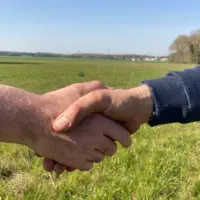 gros plan sur unepoignée de mains entre deux hommes dans un champ