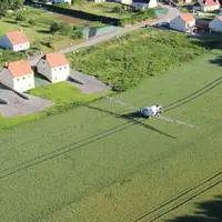 vue aérienne de maisons bordant des champs traités pas un tracteur