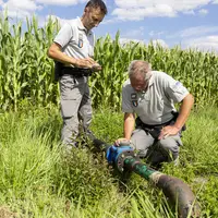 deux agents de l'OFB contrôlant un système d'irrigation devant un cham de maïs