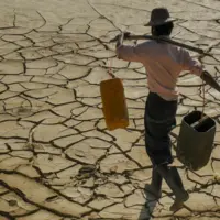 homme transportant sur ses épaules des récipients d'eau et qui marche sur un sol craquelé