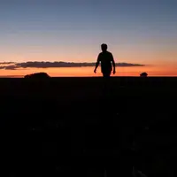 Silhouette d'une personne debout dans un champ avec un coucher de soleil.
