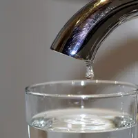 robinet avec une goutte d'eau dans un verre déjà presque rempli