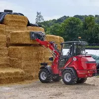 Chargeuse articlée compact électrique Hoftrac de Weidemann devant un tas de bottes de paille.