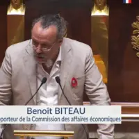 un homme à la tribune de l'assemblée nationale s'exprimant devant un micro
