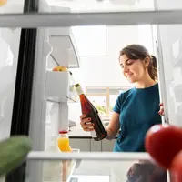 healthy eating, food and diet concept - happy woman taking orange wine bottle from fridge at home kitchen