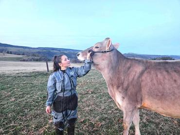 Une jeune éleveuse tient une vache brune au collet, dans une prairie vallonée.