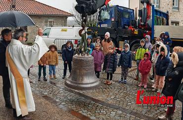 Un prêtre bénit une cloche sur le parvis de l'église, en présence d'enfants. 