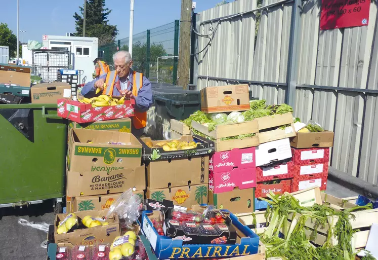 Deux hommes trient des piles de cartons remplis de fruits et légumes.