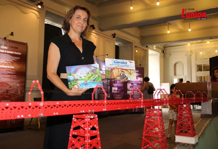 Femme tenant deux livres pour enfants devant la maquette du viaduc du Garabit