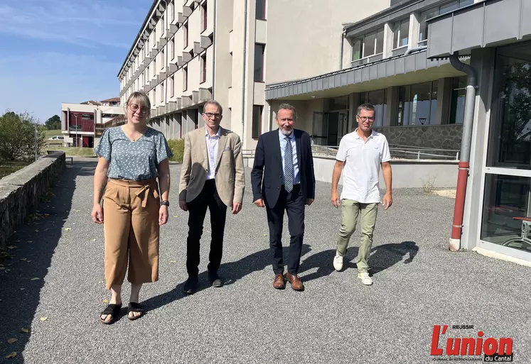 Quatre personnes, une femme et trois hommes marchant de face devant un lycée