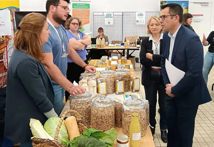 Dans une salle, au milieu d'autres personnes, deux hommes debout parlent autour d'une table avec des produits agricoles