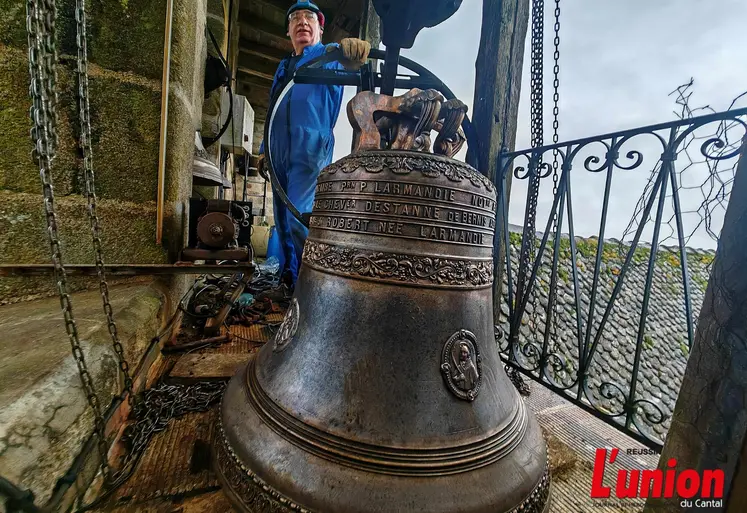 Dans un clocher, un campanaire pose fièrement devant une cloche fraîchement restaurée. 