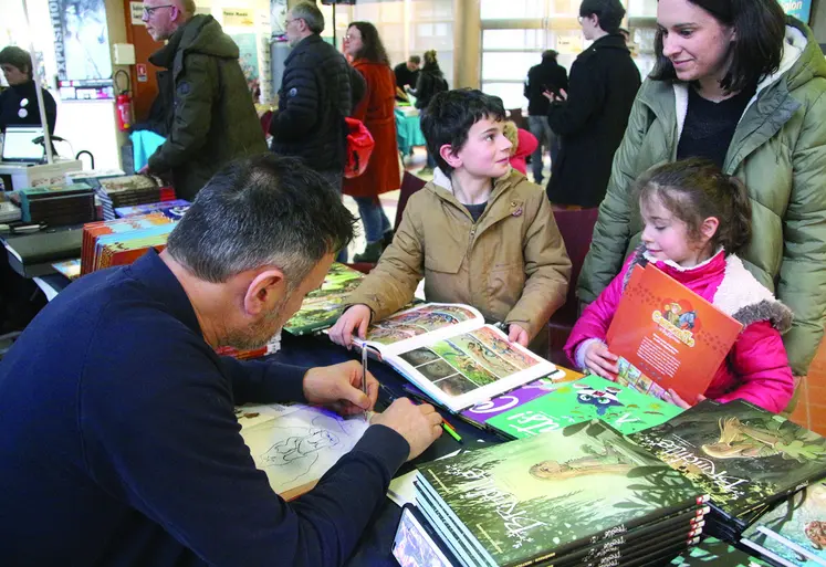 Un dessinateur en train de dédicacer une bande-dessinée à deux enfants et leur maman