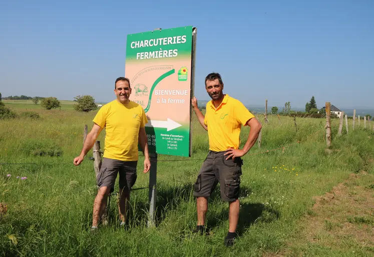 Deux hommes devant un panneau de promotion d'une exploitation agricole.