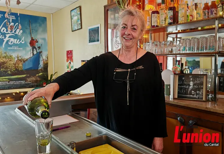 Une femme derrière un comptoir sert un verre de liqueur sur un zinc. 
