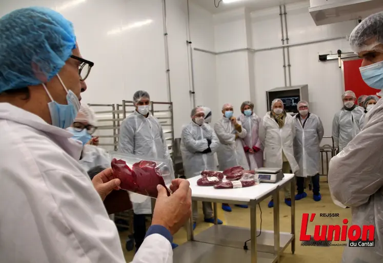 dans un atelier de découpe de viande, un responsable montre à des visiteurs un produit découpé, conditionné sous-vide