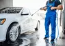 Un homme en salopette nettoie une voiture avec un jet d'eau 
