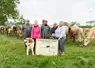 Une famille tenant un panneau devant un troupeau de vache dans la campagne