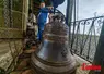 Dans un clocher, un campanaire pose fièrement devant une cloche fraîchement restaurée. 