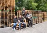 Cinq personnes posant devant des piles de palettes en bois.