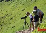 Un homme debout avec des enfants qui regardent un paysage de montagne à la longue vue.