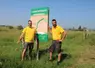Deux hommes devant un panneau de promotion d'une exploitation agricole.