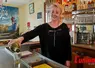 Une femme derrière un comptoir sert un verre de liqueur sur un zinc. 