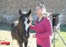 Une dame, à côté d'un cheval et avec un coq sur les épaules