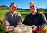 Un couple présente un plateau de fromages de chèvres, dans un paysage de campagne