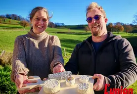 Un couple présente un plateau de fromages de chèvres, dans un paysage de campagne