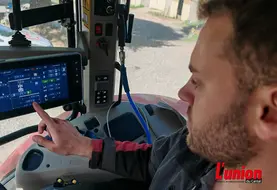 agriculteur dans la cabine de son tracteur pilote l'autoguidage sur un écran tactile.