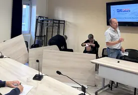Tables renversées dans une salle de réunion, avec Christian Arvis s'adressant à une personne hors cadre avec une véhémence gestuelle visible.