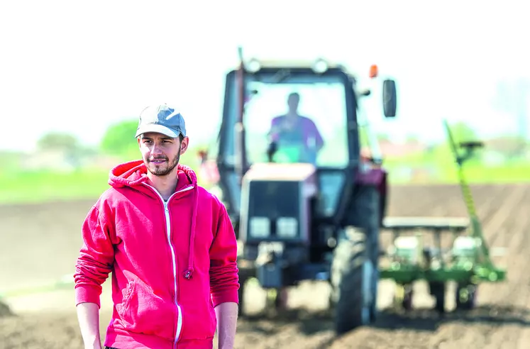 Jeune agriculteur dans un champ devant un tracteur