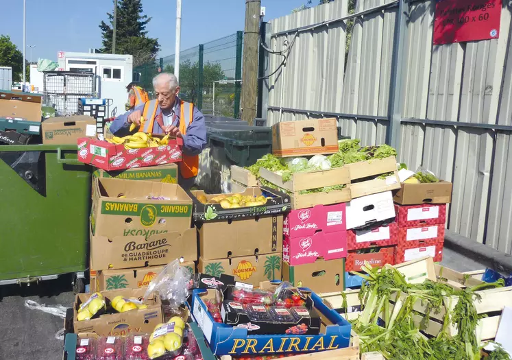 Deux hommes trient des piles de cartons remplis de fruits et légumes.